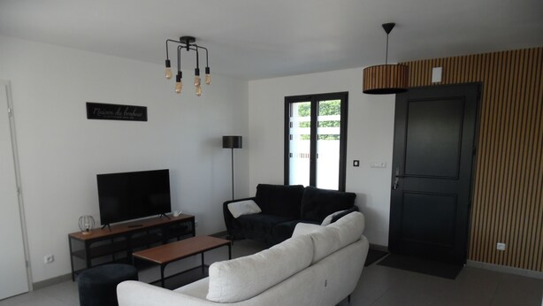 A modern living room with a white sofa, a flat-screen TV, a coffee table, and a black armchair. - La Villa « Jules Verne » à Saint Firmin - Le Crotoy, au Cœur de la Baie de Somme (Le Crotoy)