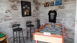 A room with a brick wall, a foosball table, two bar stools, and a framed poster. - La Villa « Jules Verne » à Saint Firmin - Le Crotoy, au Cœur de la Baie de Somme (Le Crotoy)