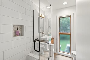 A modern bathroom with a glass shower enclosure, a white sink, and a window with blinds.
