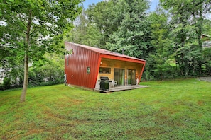 Une petite cabane en bois rouge, dotée d’un porche abrité et entourée d’une végétation luxuriante.