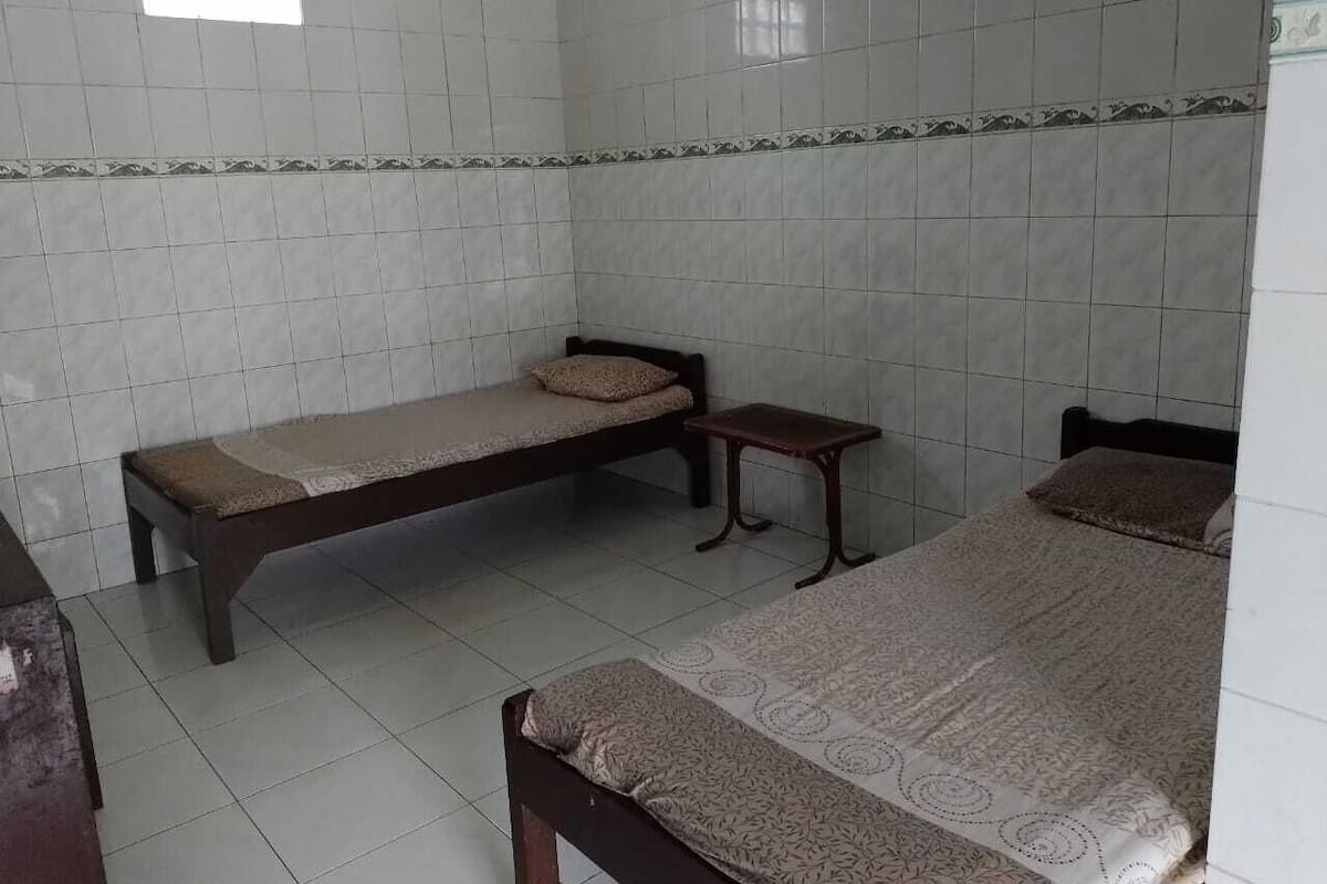 A room with two single beds, a small table, and tiled walls.