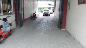 Un pasillo estrecho con suelo de baldosas, un scooter estacionado y un coche a lo lejos.