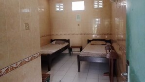Una habitación con dos camas de madera, paredes de azulejos, un ventanal pequeño y un ventilador de techo.