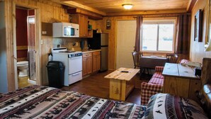 Un interior de cabaña con kitchenette, comedor y cama.