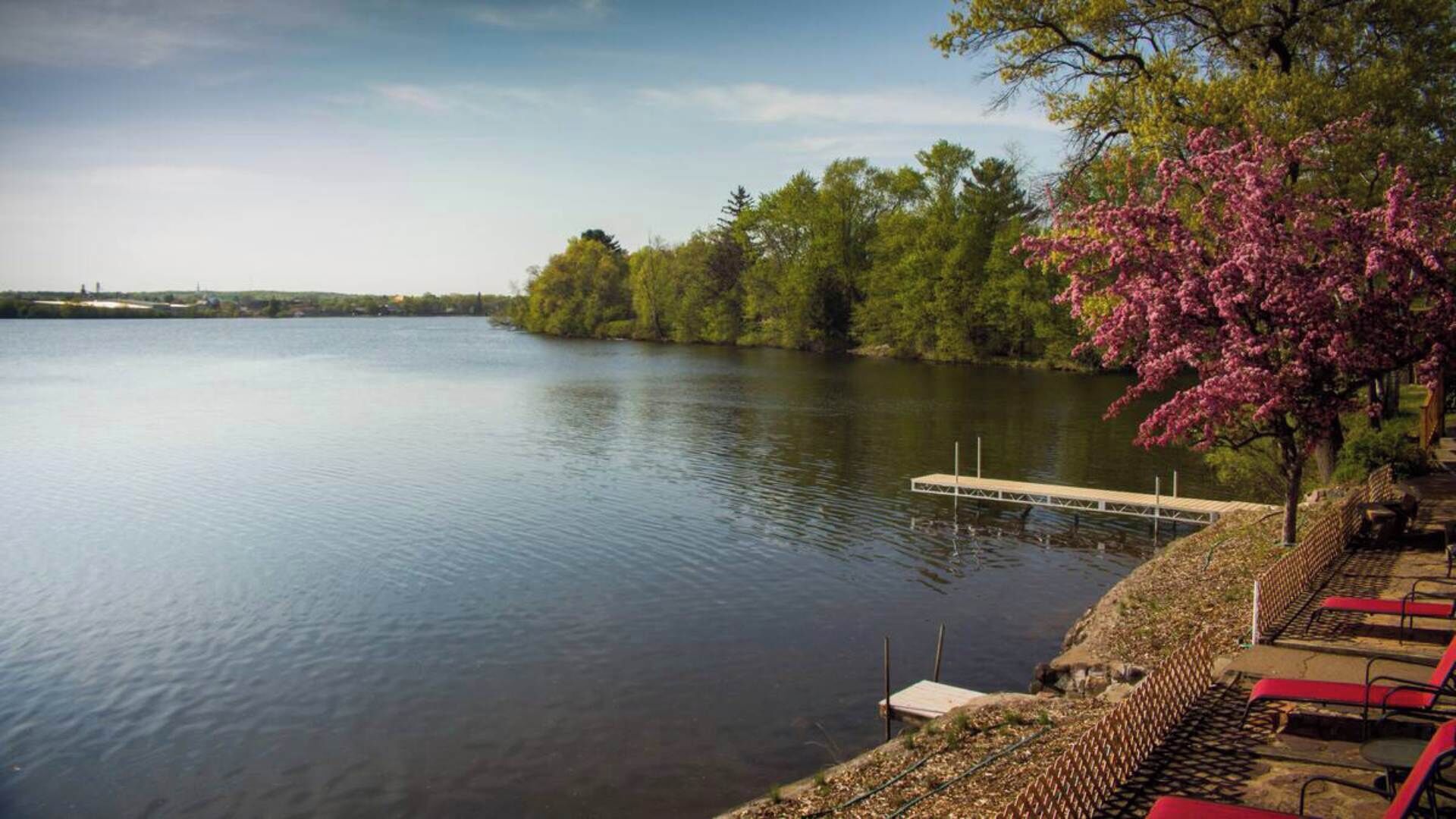 Un lac paisible avec une jetée qui s’avance sur l’eau, entouré d’arbres et sous un ciel dégagé.