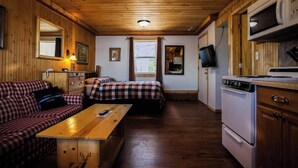Una cabaña con dos camas, una mesa de comedor, una cocina con estufa y un televisor.