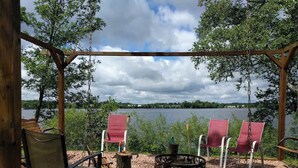 Una terraza de madera con un banco y dos sillas rojas mirando un lago.