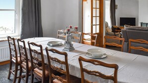 Un comedor con una mesa preparada para cuatro personas, sillas de madera, un candelabro y un televisor al fondo.