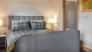 Un dormitorio con una cama tapizada en gris, un cabecero, dos lámparas de noche y una puerta con espejo.