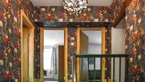Una habitación con papel tapiz floral, un marco de puerta de madera, una barandilla verde y una lámpara colgante.
