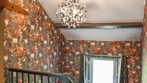 Una escalera con papel tapiz floral, barandal de madera y una lámpara moderna.