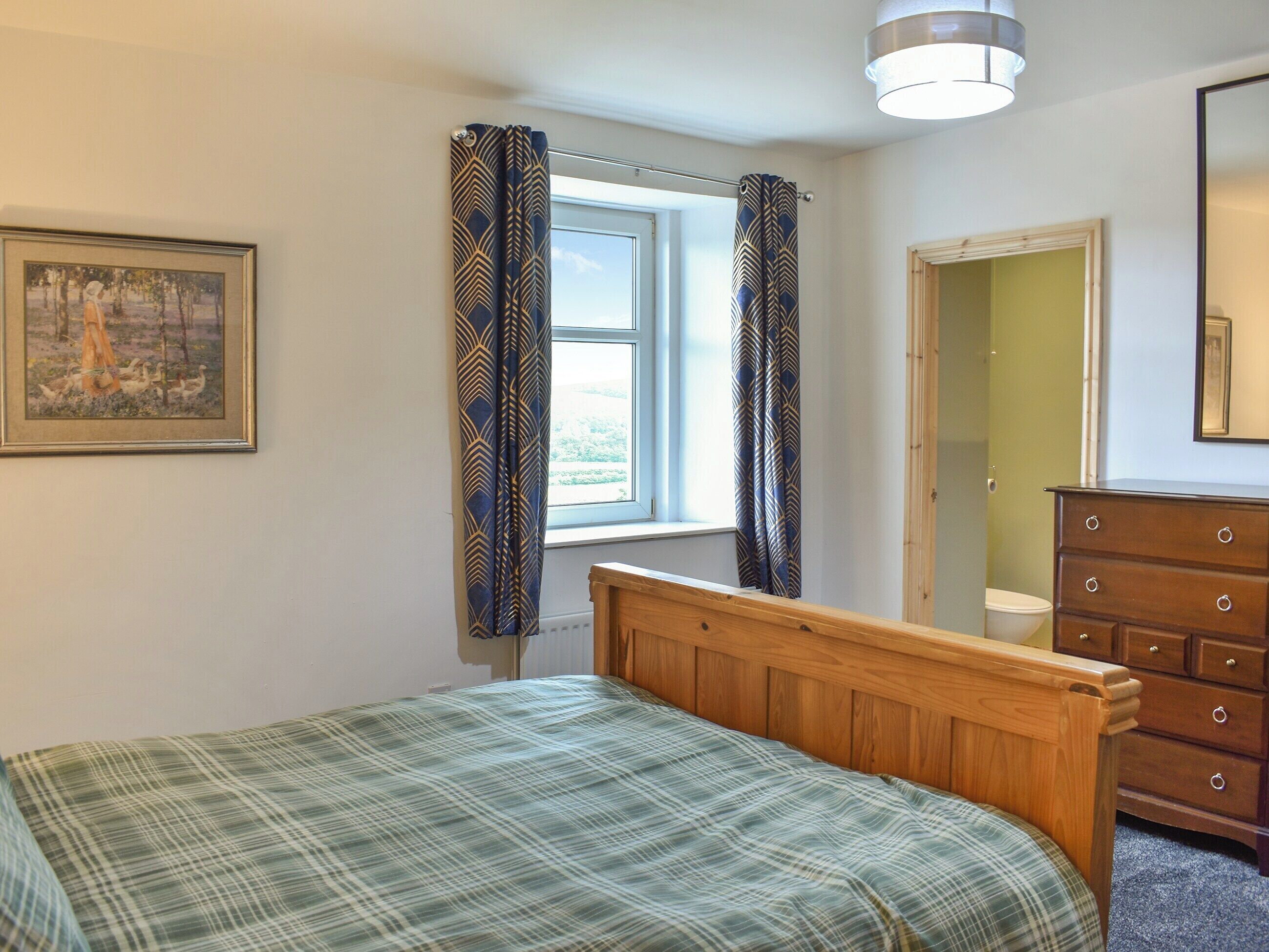 A bedroom with a bed, a dresser, a window with curtains, and a painting on the wall.