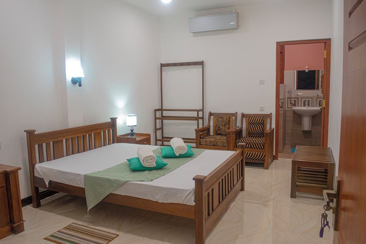 A neatly arranged bedroom with a wooden bed, a bedside table, a chair, a small table, and a mirror.