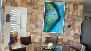 Ein Essbereich mit einem runden Glastisch, Korbstühlen, einem Deckenventilator und einer Steinwand mit einem großen Fischgemälde.