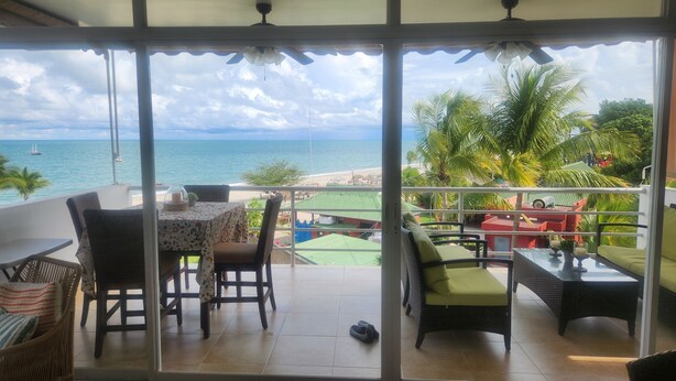 Ein Balkon mit Tisch und Stühlen, einer Couch und Blick auf Strand und Meer.