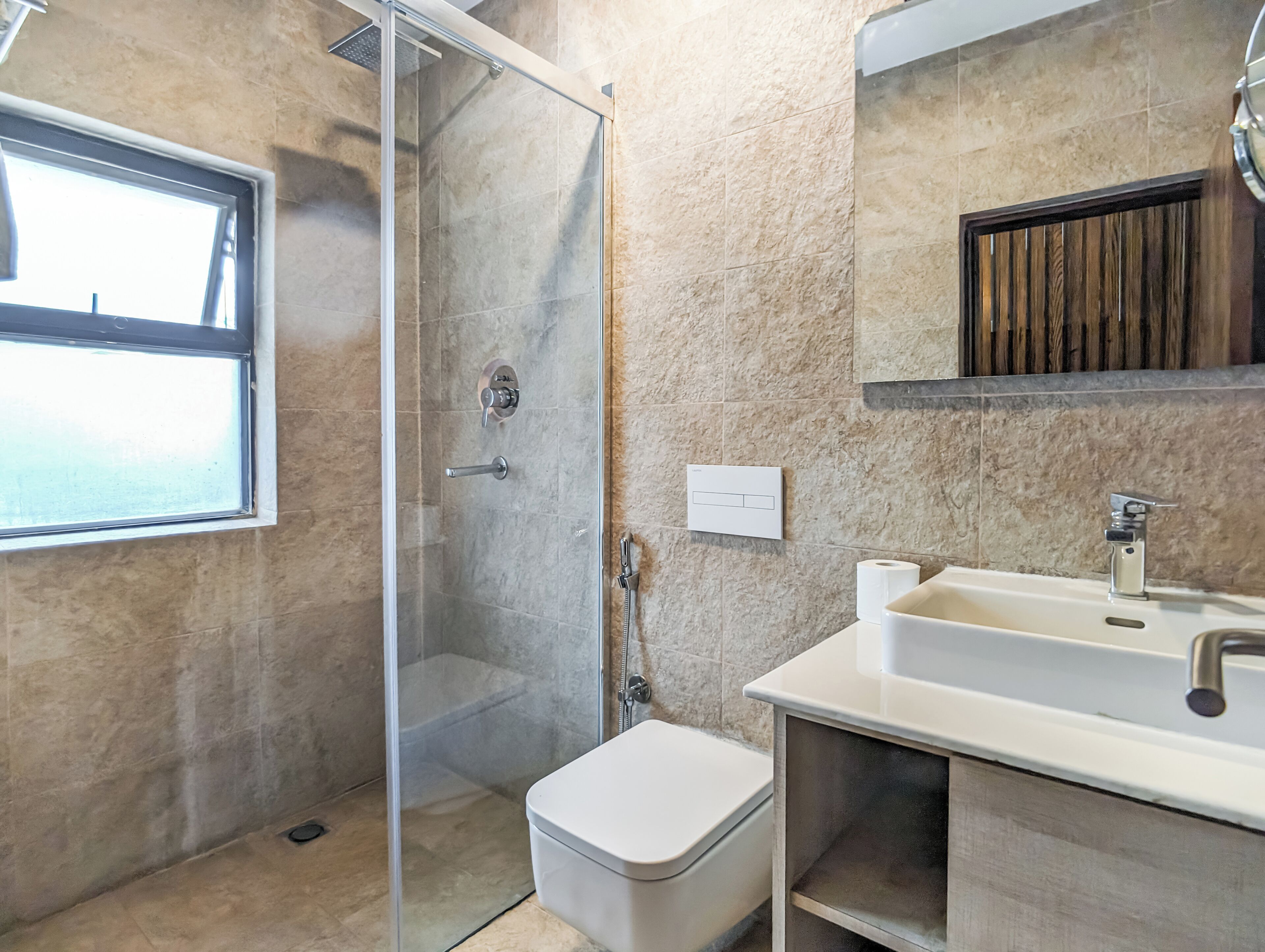 A bathroom with a glass-enclosed shower, a toilet, a sink, and a window.