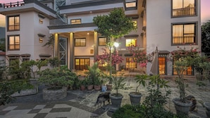 A modern building with multiple balconies, a courtyard with potted plants, and a staircase leading to the upper floors. - Uma Residence & Suites (Nagarjun)