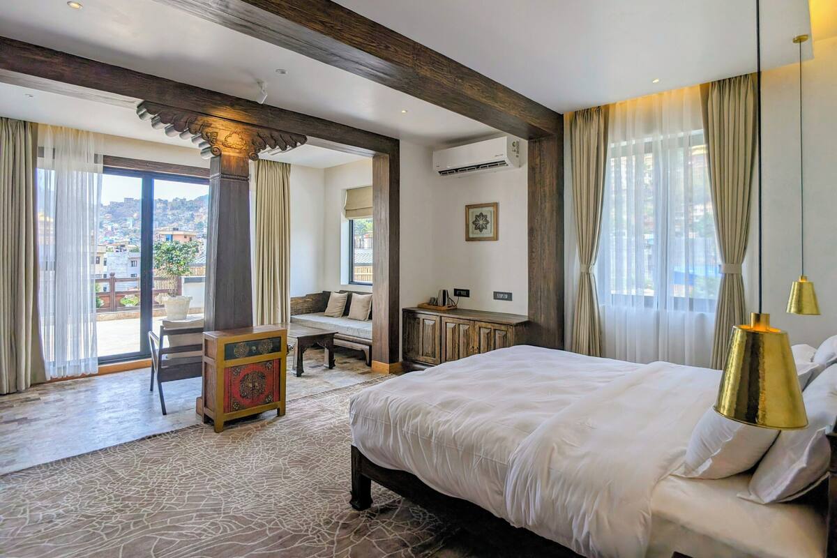 A hotel room with a large bed, a desk, a chair, a small table, and a view of the city.