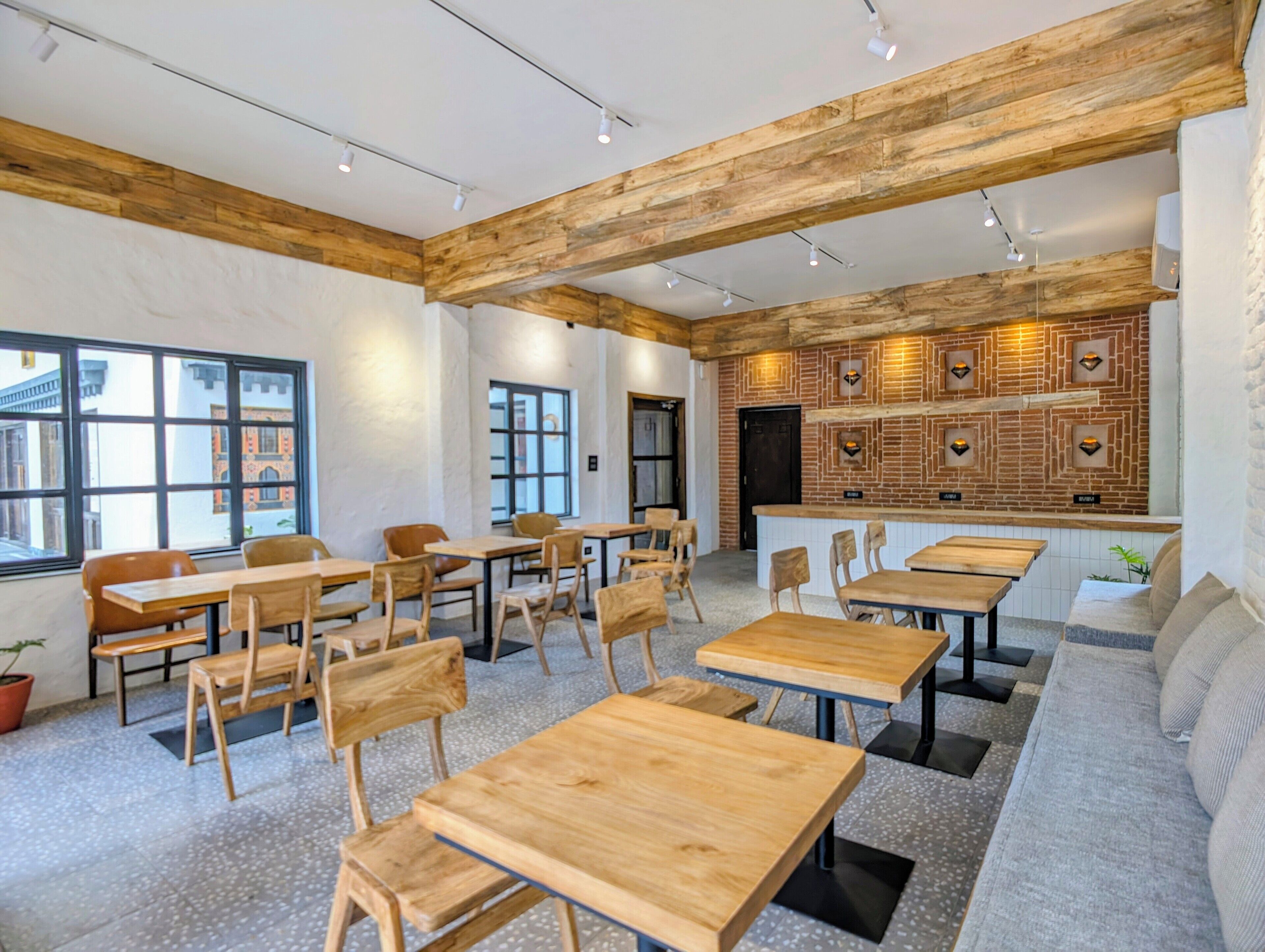 A modern interior with wooden tables and chairs, a brick wall with geometric patterns, and a seating area with a sofa.
