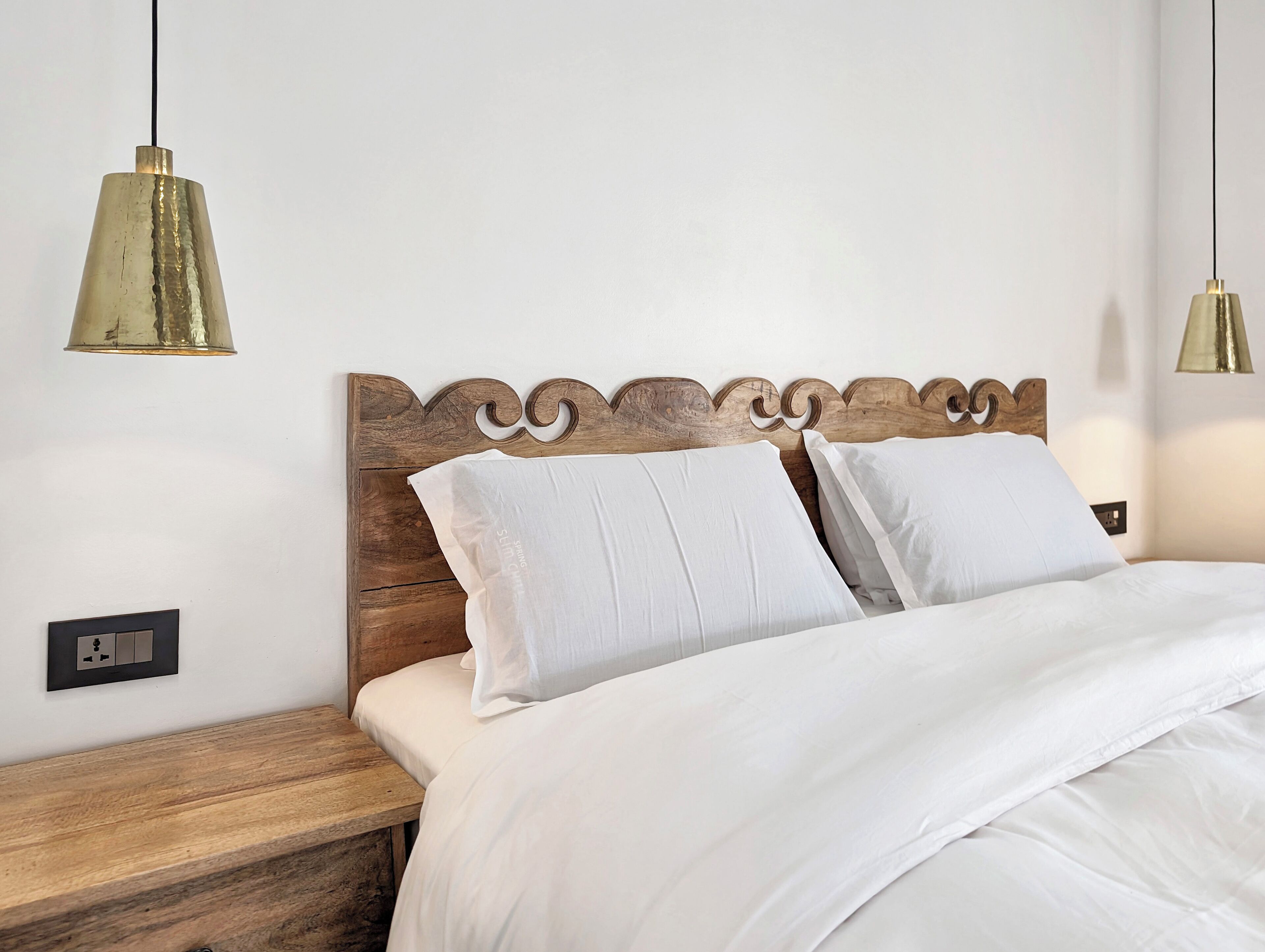A neatly made bed with a wooden headboard, two bedside tables, and two pendant lights.