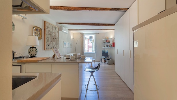 Une cuisine étroite avec des poutres en bois, un coin repas avec un tabouret de bar et une vue sur la rue par une fenêtre.