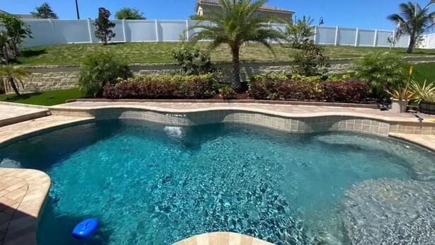 A swimming pool with a curved edge, surrounded by a white fence, palm trees, and a building in the background. - Private pool-Comfy home- 8 guest

 (Davenport)