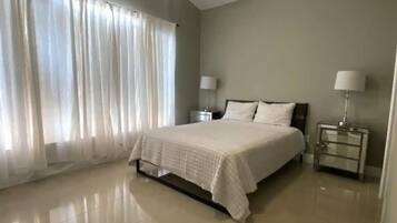 Un dormitorio amplio con una cama grande, un ventilador de techo y dos mesitas de noche con lámparas.
