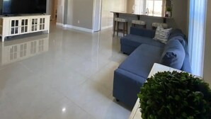 A spacious living room with a large TV, a blue sofa, and a wooden cabinet. - Private pool-Comfy home- 8 guest

 (Davenport)