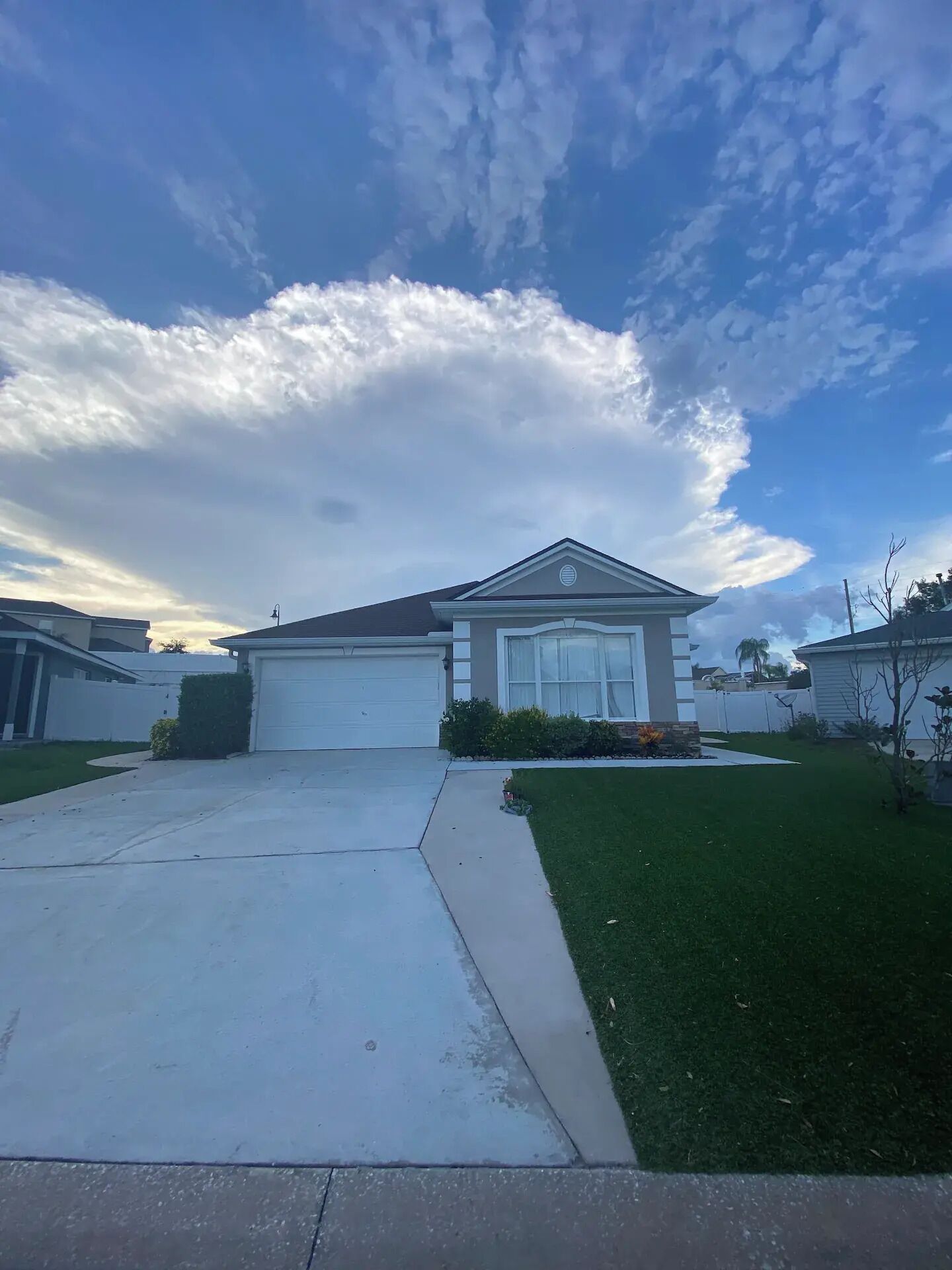 A suburban house with a garage, a well-maintained lawn, and a clear sky with clouds.