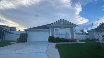 A suburban house with a garage, a well-maintained lawn, and a clear sky with clouds.