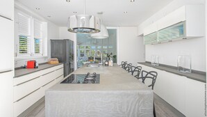Een moderne keuken met een centraal kookeiland, roestvrijstalen apparatuur en een hanglamp.