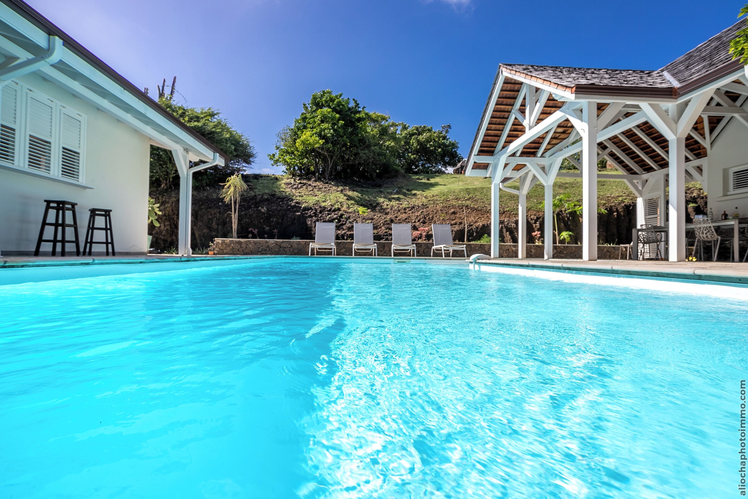 A clear blue swimming pool with lounge chairs and a covered patio area.