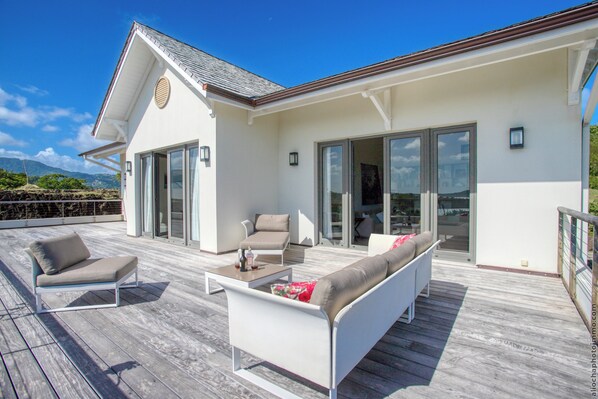 A modern house with a deck featuring outdoor furniture, large glass doors, and a view of the landscape.
