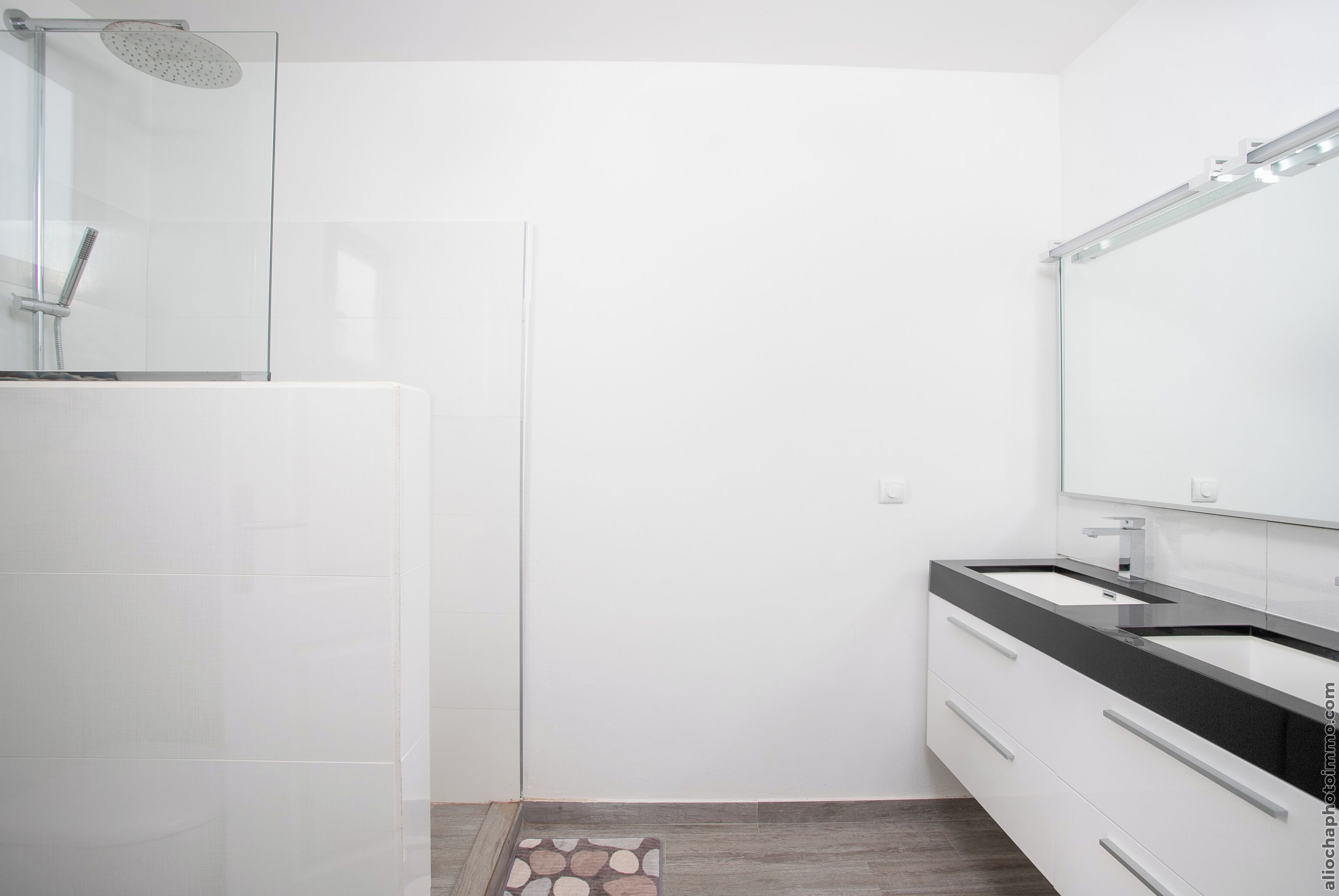 A modern bathroom with a glass shower enclosure, a white vanity with a black countertop, and a large mirror.