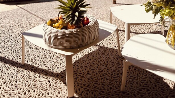 Un área junto a la piscina con sillones reclinables, una cesta de mimbre con fruta y una mesa con un florero.