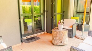 A patio area with a sliding glass door leading to a garden, a round wooden table with a potted plant, and wicker furniture. - Lugana Lovers - Italian Homing (Sirmione)