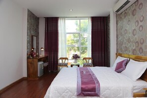 A hotel room with a large bed, a desk with a computer, two chairs, and a window with curtains. - Red Diamond Hotel DN- by Bay Luxury (Da Nang)