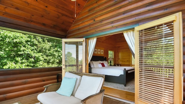 A wooden cabin with a cozy interior, a bed with a white headboard, and a wicker sofa with cushions. - Mountain Retreat Hot Tub & Game Room Pets Friendly (Mineral Bluff)