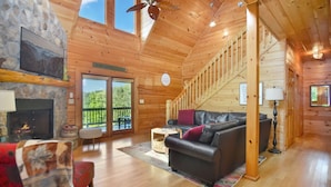 A cozy cabin interior with a fireplace, leather sofa, and a staircase leading to a balcony. - Mountain Retreat Hot Tub & Game Room Pets Friendly (Mineral Bluff)