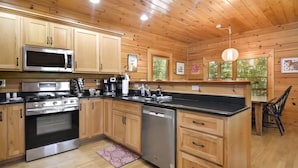A kitchen with wooden cabinets, a stainless steel microwave, an oven, a dishwasher, and a black countertop. - Mountain Retreat Hot Tub & Game Room Pets Friendly (Mineral Bluff)