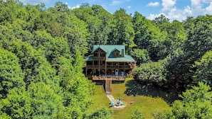 A wooden cabin with a green roof, surrounded by dense forest. - Mountain Retreat Hot Tub & Game Room Pets Friendly (Mineral Bluff)