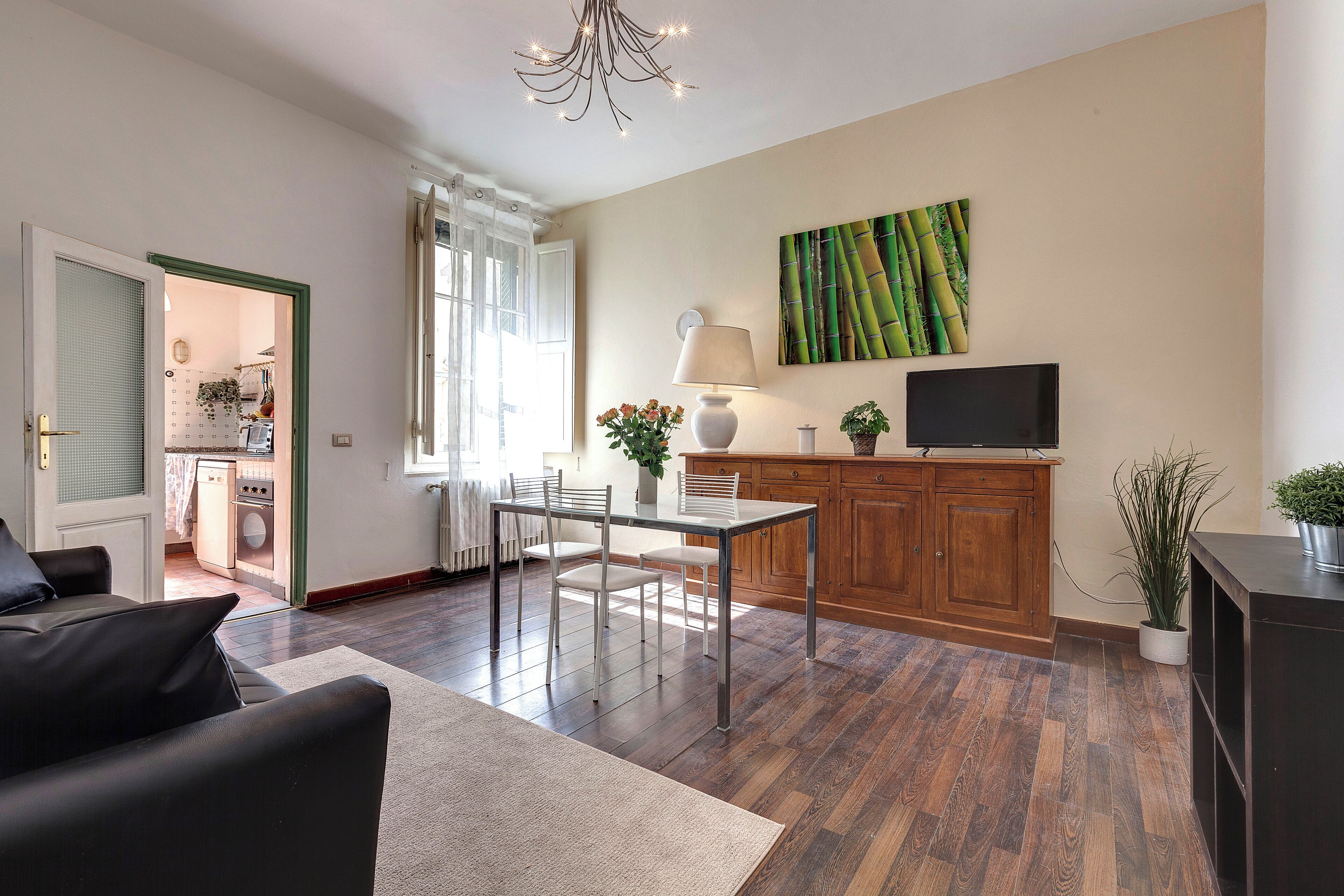 Un salon moderne comprenant un canapé, une table à manger avec des chaises, un téléviseur et un coin cuisine visible à travers une porte ouverte.