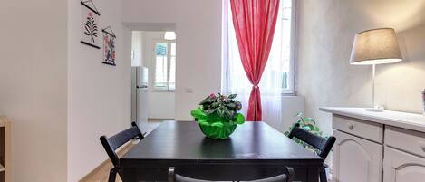 A dining area with a table, chairs, a green plant, a red curtain, and a lamp.