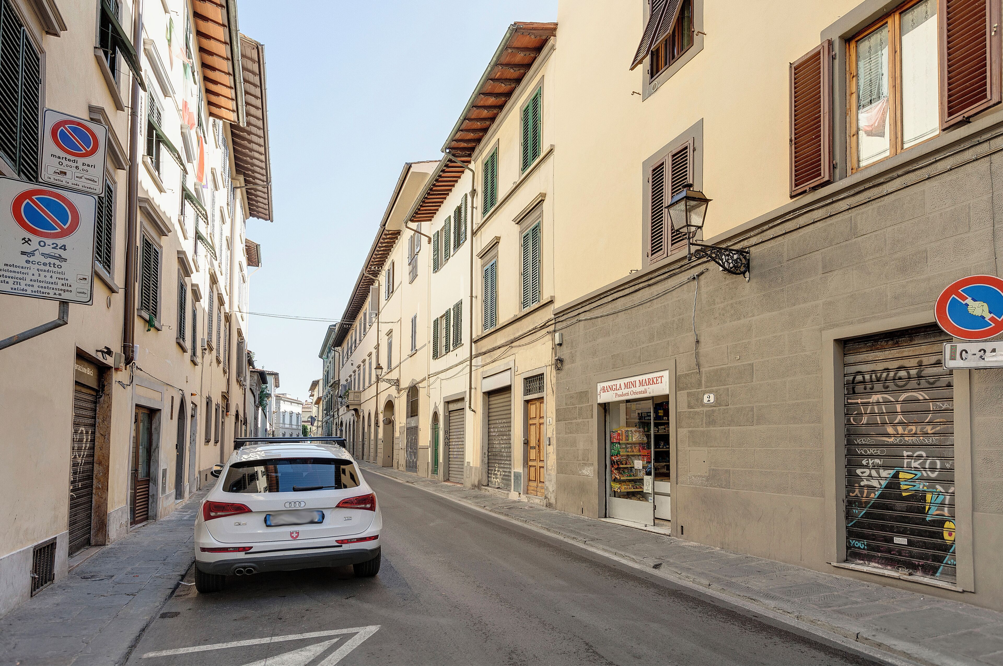 A narrow street with buildings on both sides, a parked white car, and closed shop shutters.