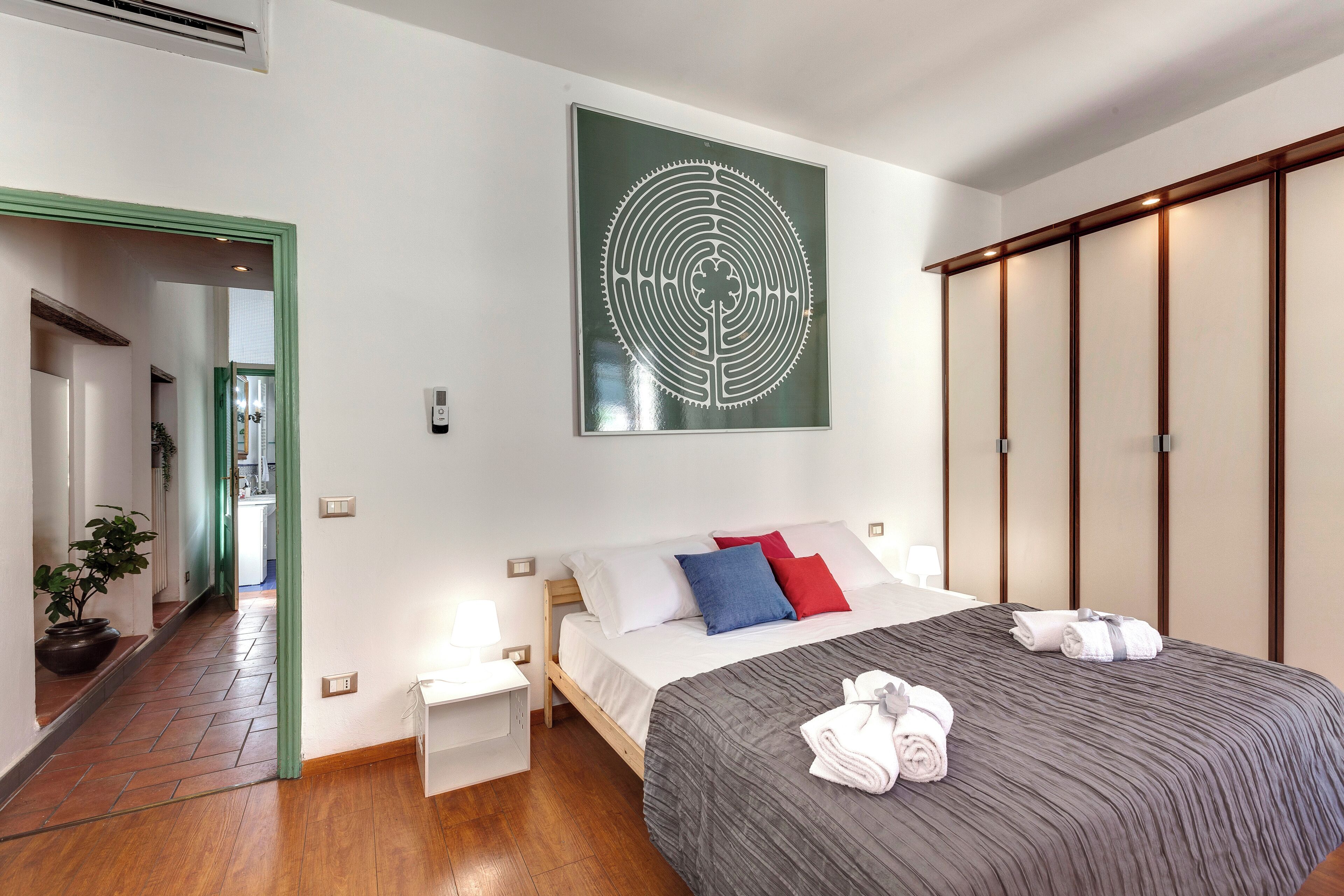 A hotel room with a bed, a green-framed door, a wall-mounted artwork, and a wooden wardrobe.