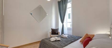 A bedroom with a bed, a chair, a window with curtains, and a hanging light fixture.