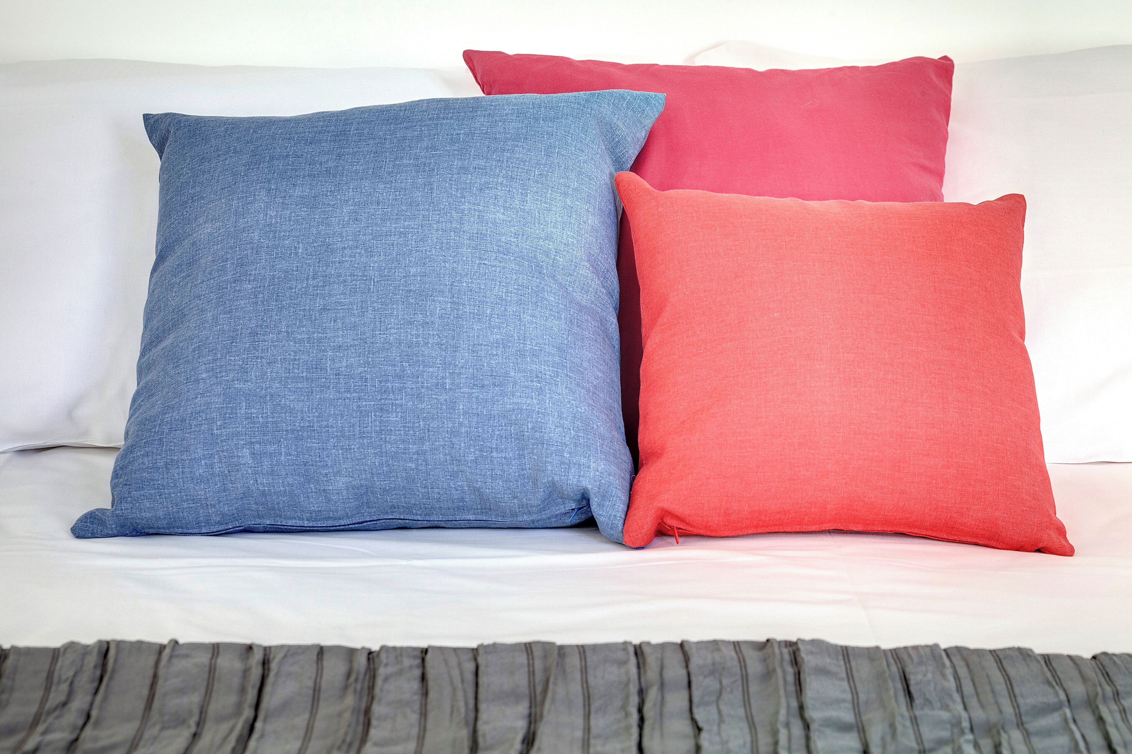A bed with a white sheet and two pillows, one blue and one red.