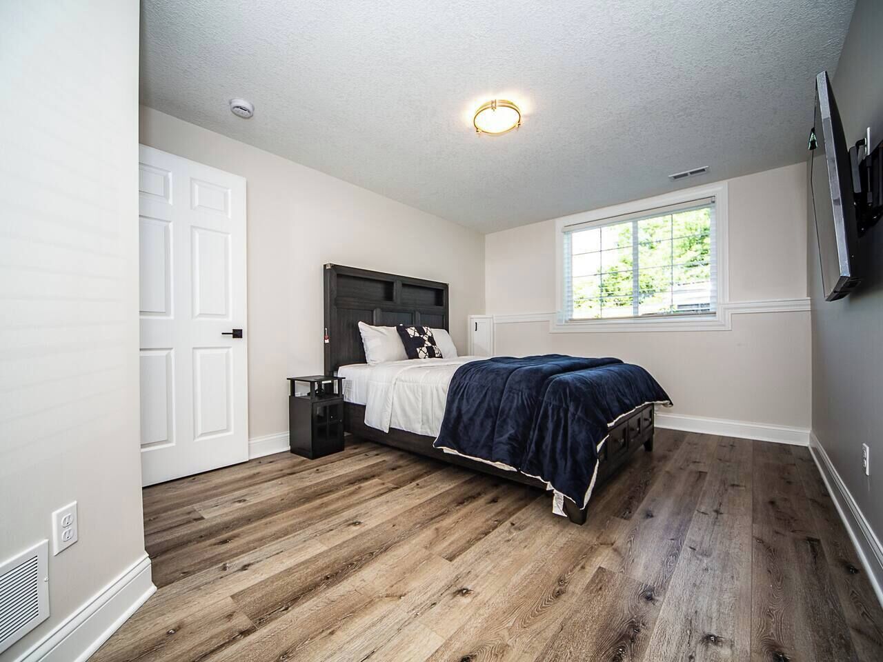 A bedroom with a bed, a window, a door, and a ceiling light.