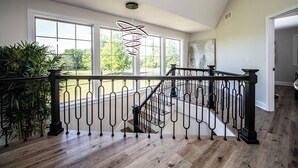 A spacious room with a wooden floor, large windows, and a black metal railing.
