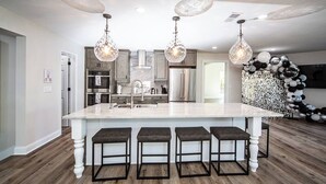 A modern kitchen with a large island, bar stools, pendant lights, and a decorative balloon arch.